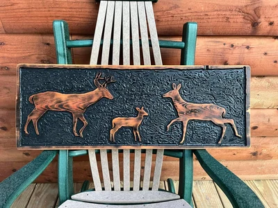 Carved relief panel of a buck, doe and fawn against a textured black background