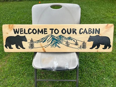 Carved Welcome To Our Cabin sign with bears, pines and blue mountains